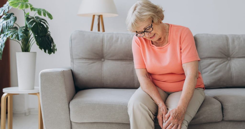 À QUI S'ADRESSENT MES SOINS ? PERSONNE AGÉE ASSISE SUR UN CANAPÉ SE MASSANT LE GENOUX